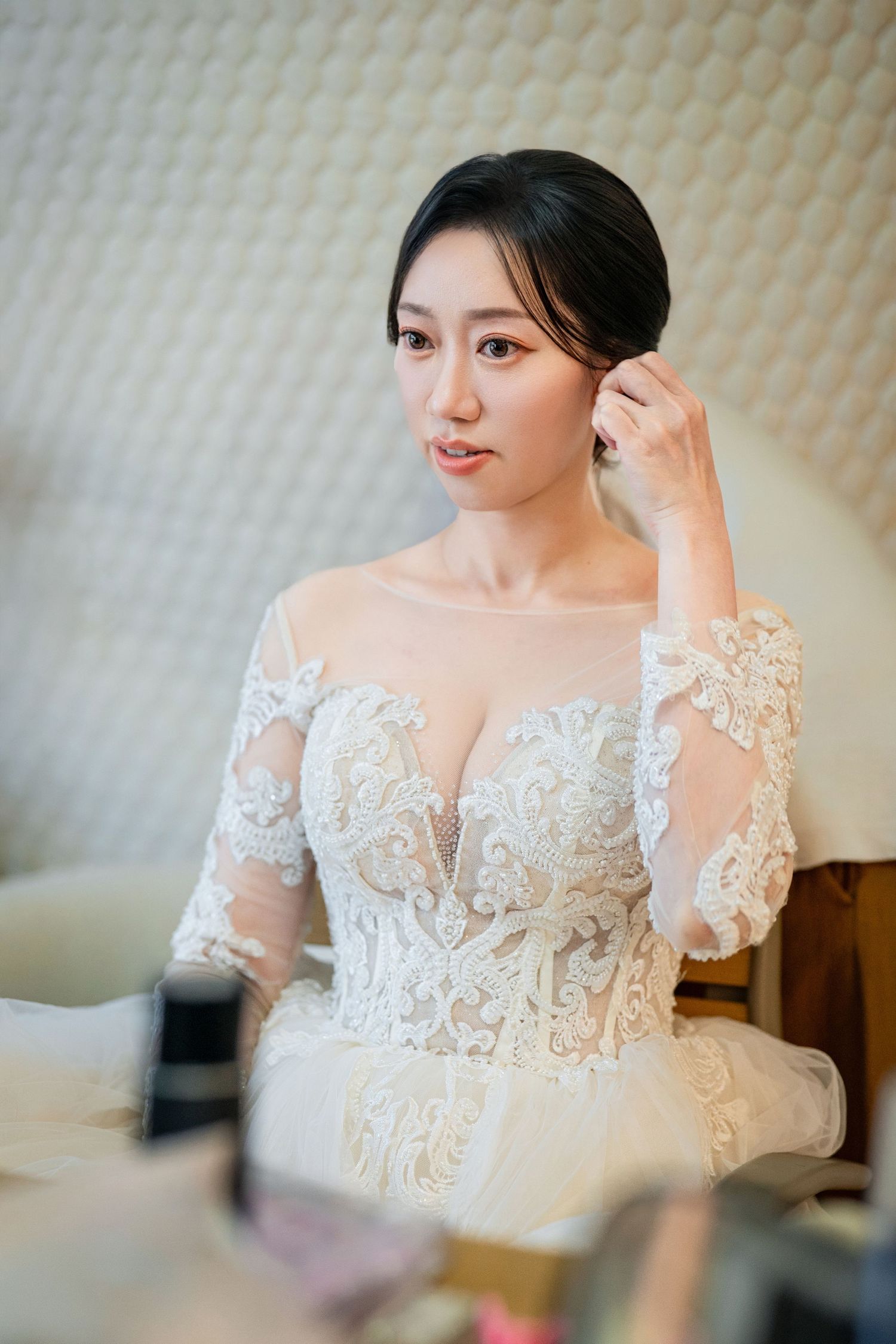 Close up details of delicate white lace embroidery on a bridal gown with sheer sleeves and floral appliques.
