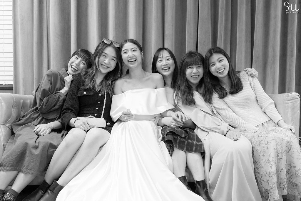 Black and white photo of bride with friends sitting together on couch.