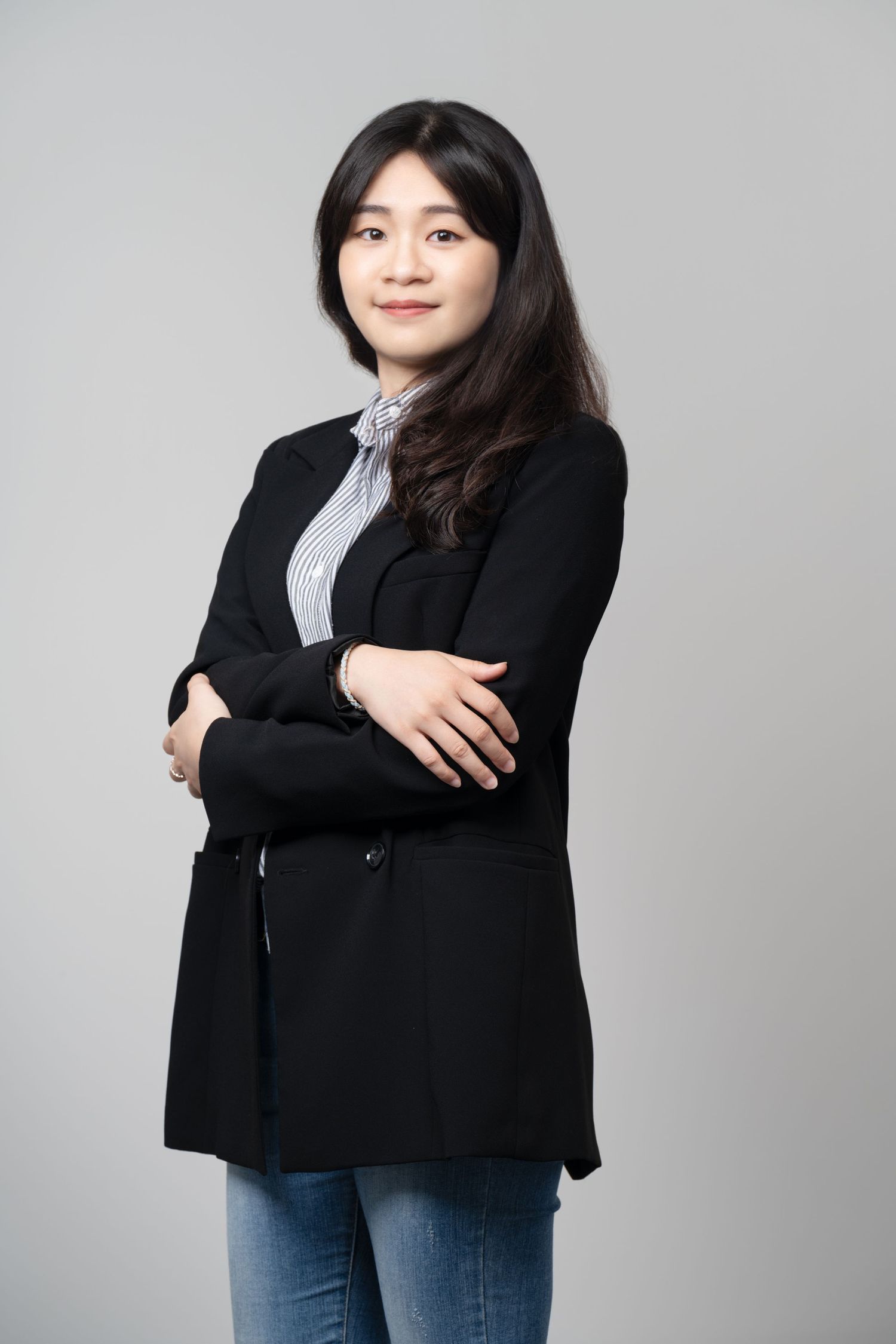 Professional portrait of someone wearing a black cardigan and striped shirt against a gray background.