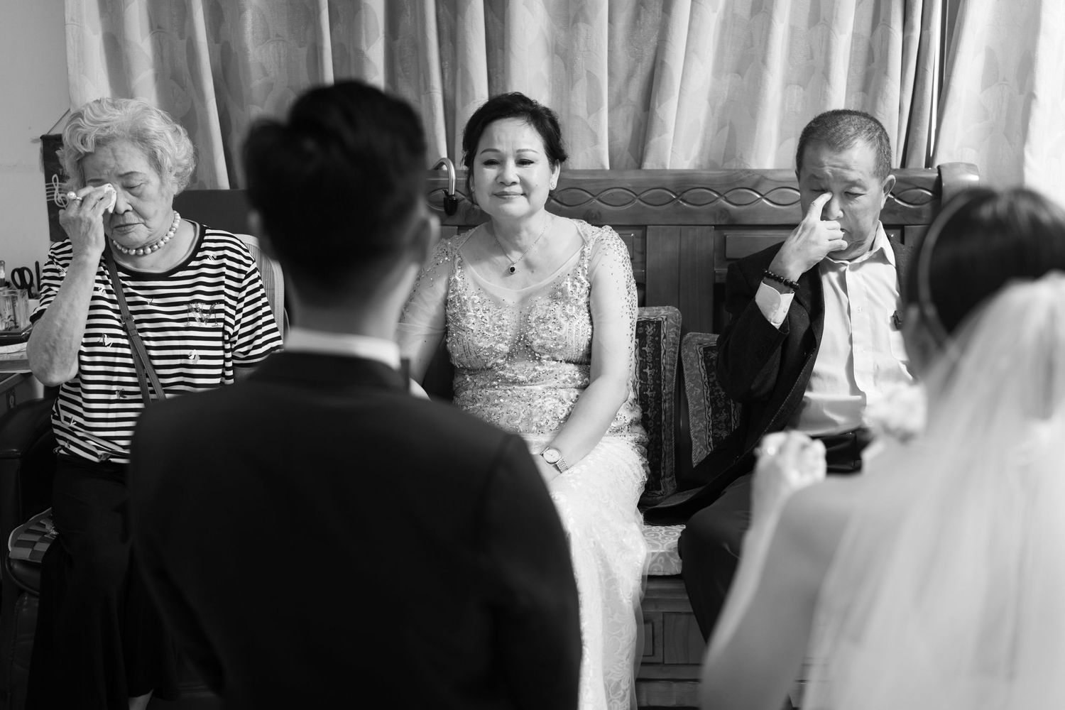 Black and white photo of an emotional wedding ceremony with guests wiping away tears during a tender moment.