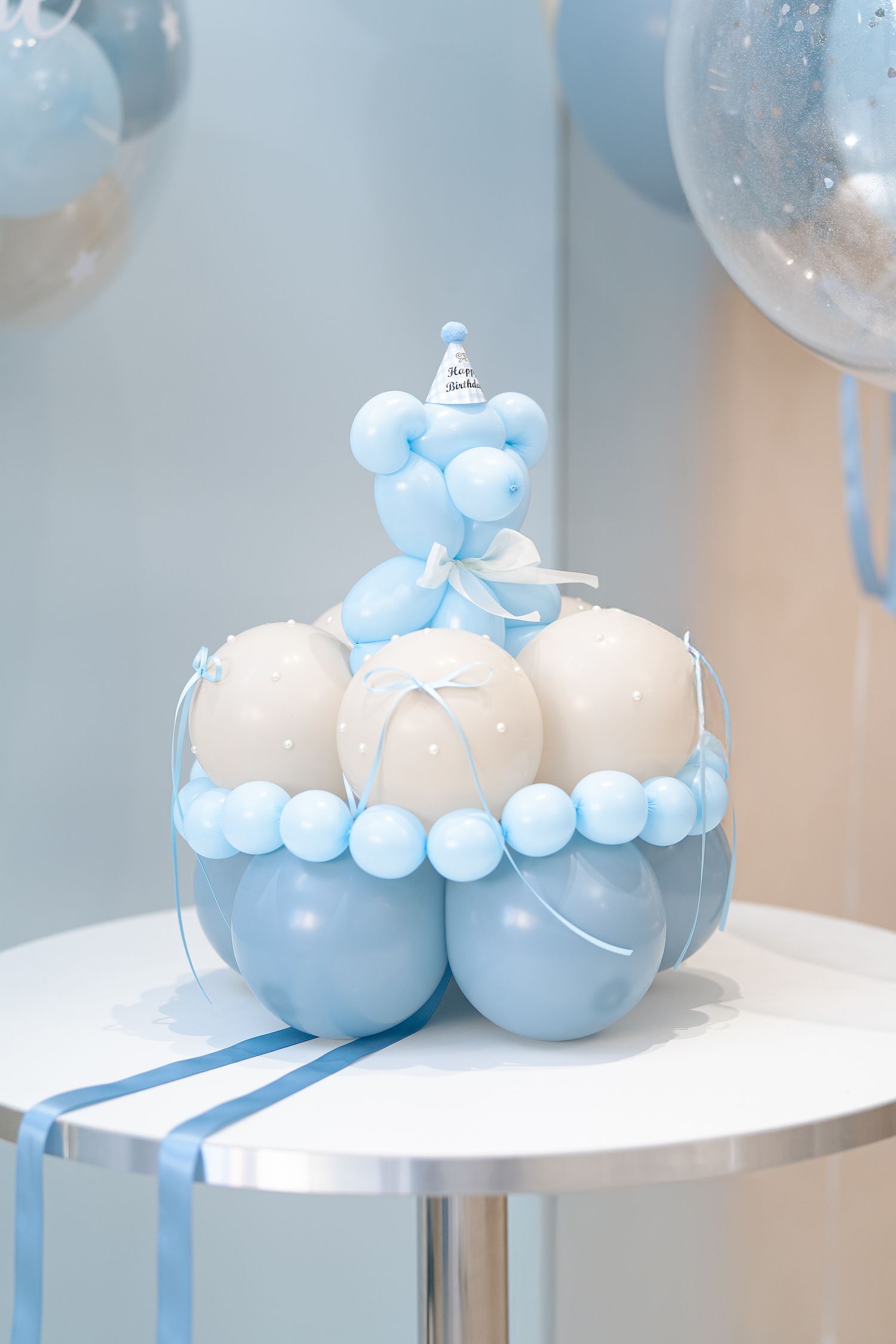 Light blue and white balloon arrangements create an elegant party decoration display on white pedestals.