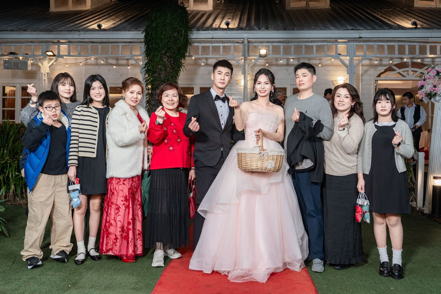 A group gathers on a red carpet at an elegant evening wedding reception venue with decorative lighting.