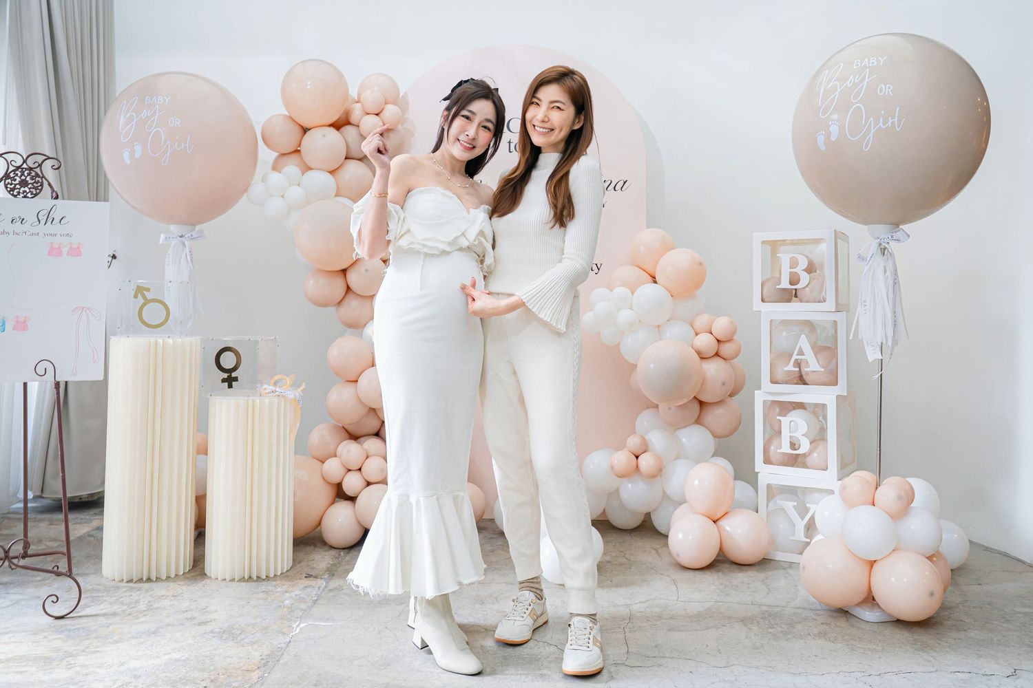 Elegant baby shower celebration setup with peach and white balloons, framed photos, and floral decorations in a bright room.