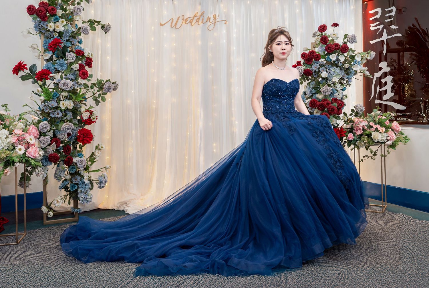 A stunning navy blue ballgown with a flowing train is showcased against a rustic backdrop with red rose decorations.