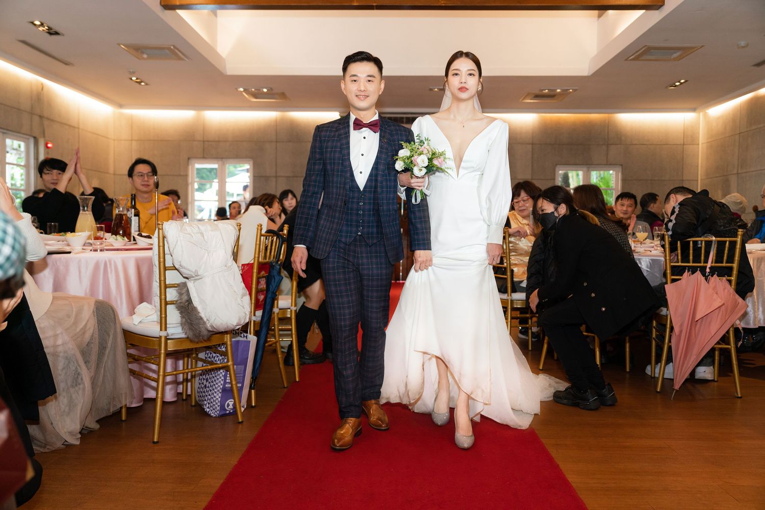 A wedding couple makes their entrance on a red carpet in an elegant reception venue with warm lighting and seated guests.