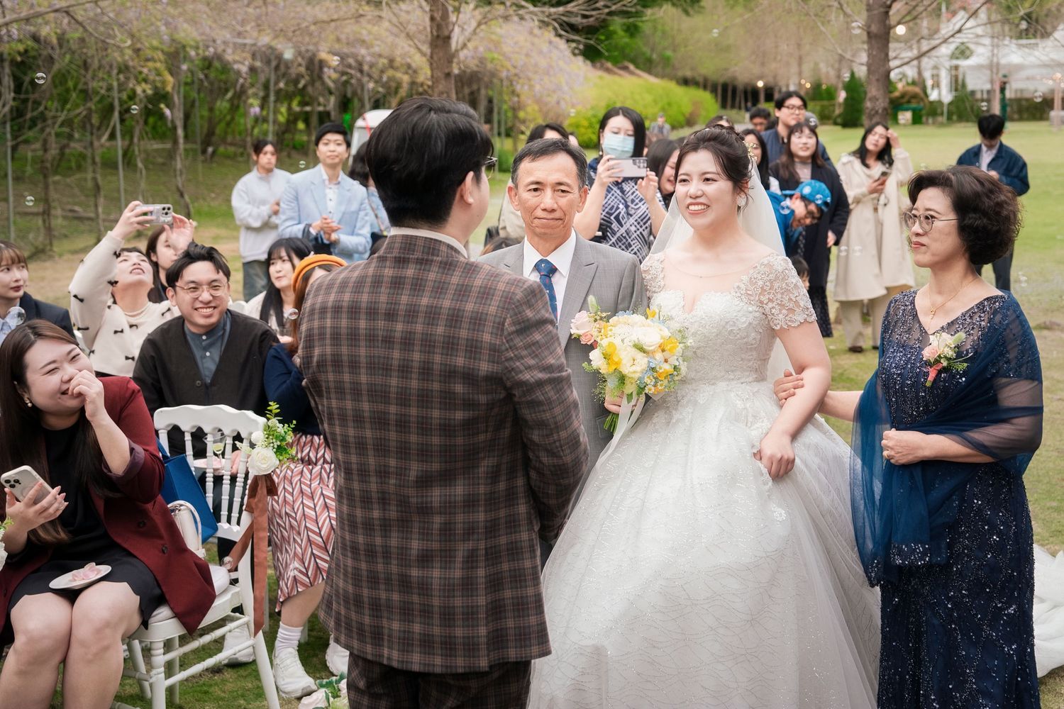 Wedding guests dance and celebrate together during an outdoor reception in a garden setting.