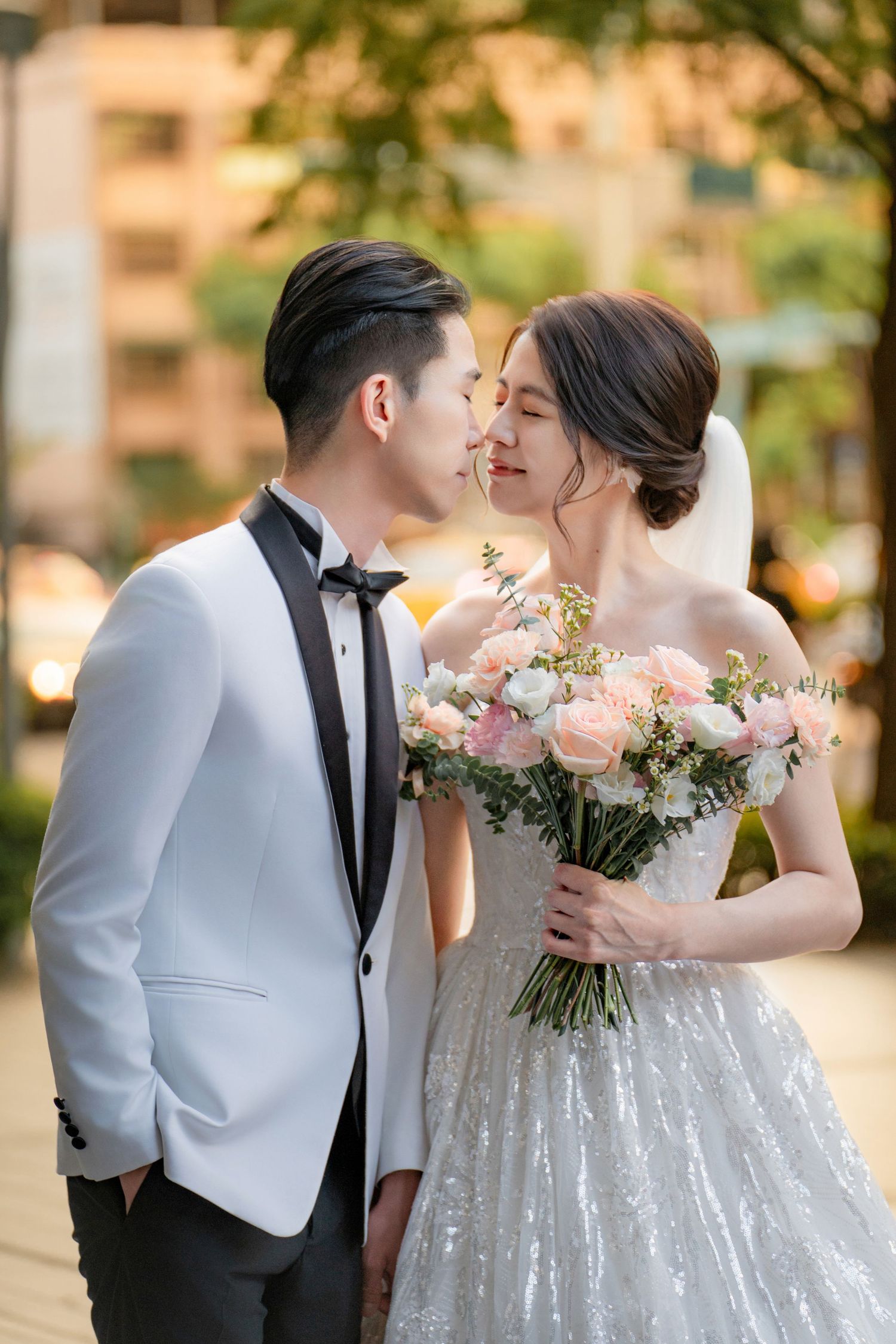 Romantic wedding portrait showcasing the bride in a sparkling gown holding a pink bouquet with the groom in a white jacket.