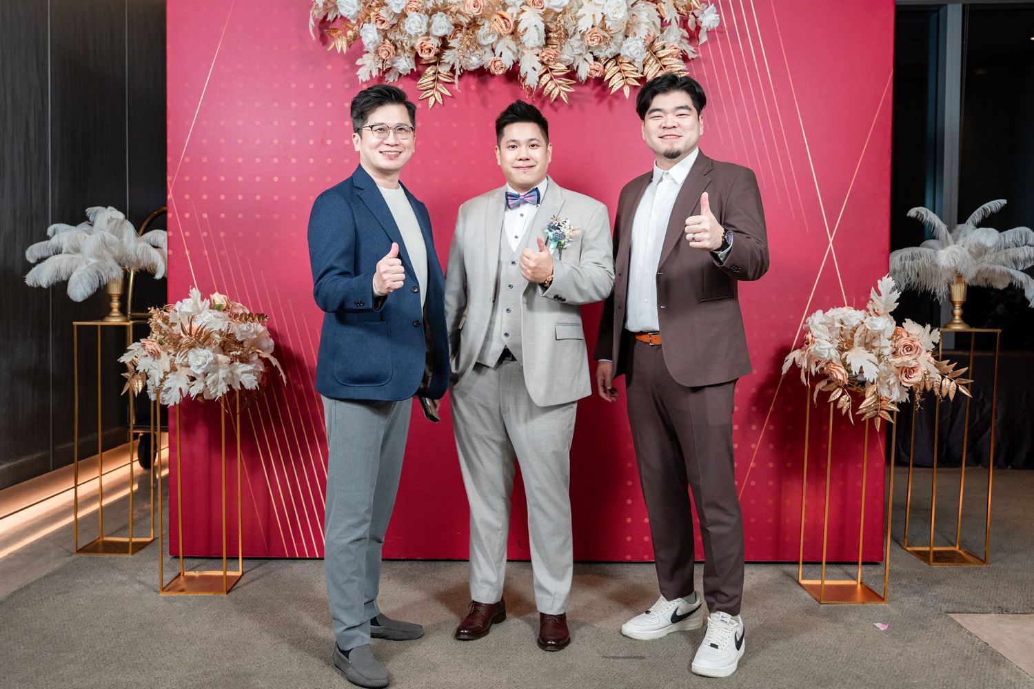 Wedding party members in formal attire posing against a pink backdrop with floral decorations.