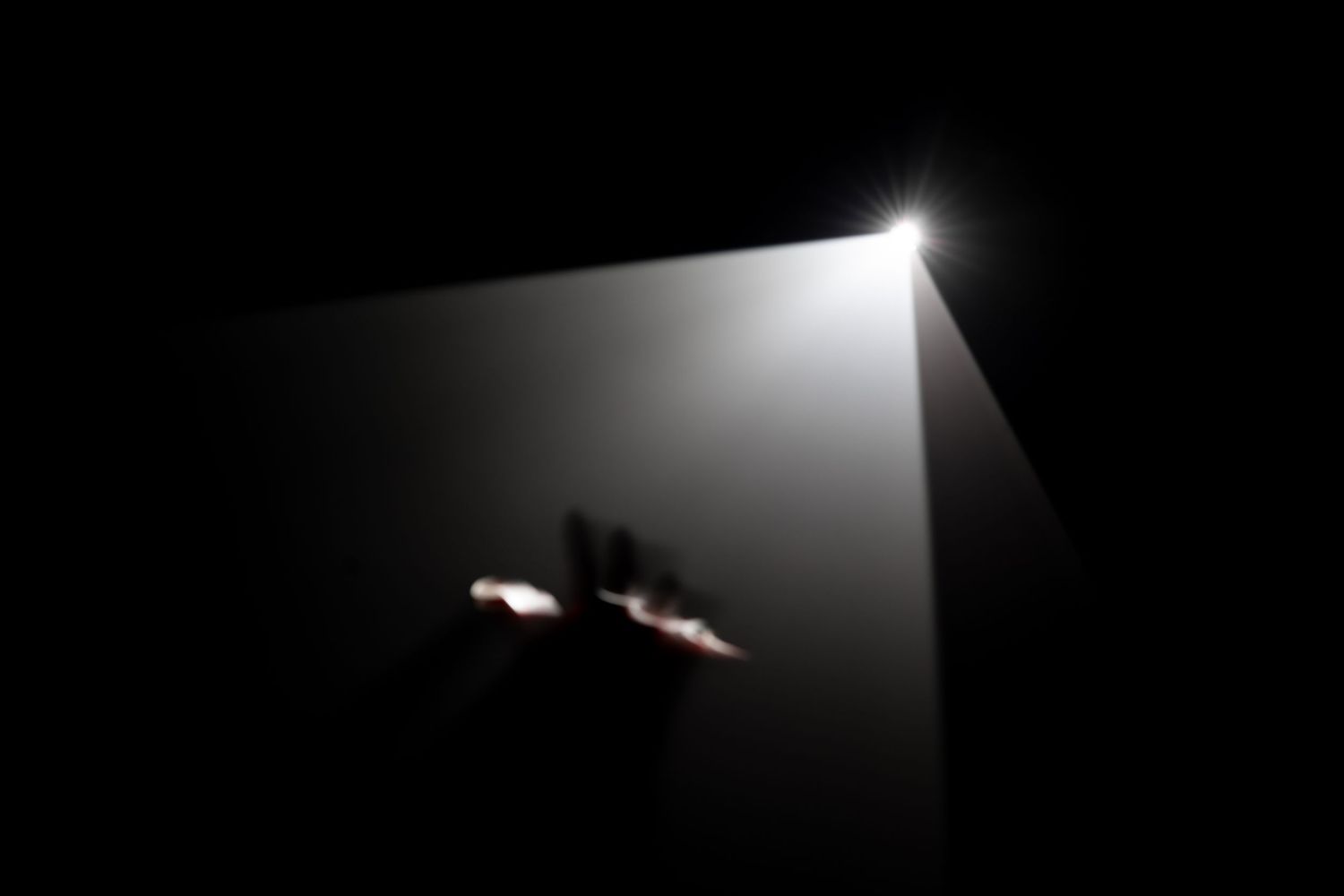 Dramatic beam of light piercing through darkness with silhouetted hands reaching toward the glowing source.