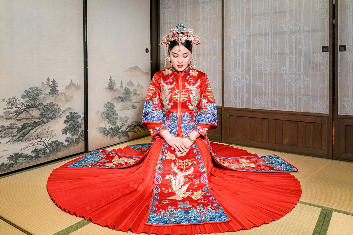 A person in a red traditional Chinese wedding dress with blue embroidery sits on tatami floor in a Japanese room.