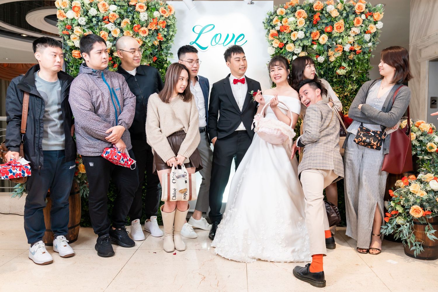 Intimate wedding group portrait with casual poses against a peachy floral backdrop.