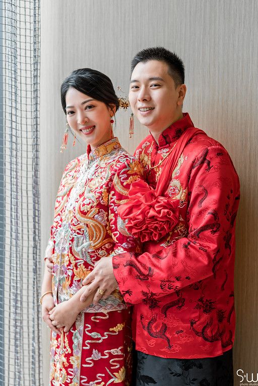 A couple wearing traditional Chinese wedding attire pose together in red and white qipao and tang suit.