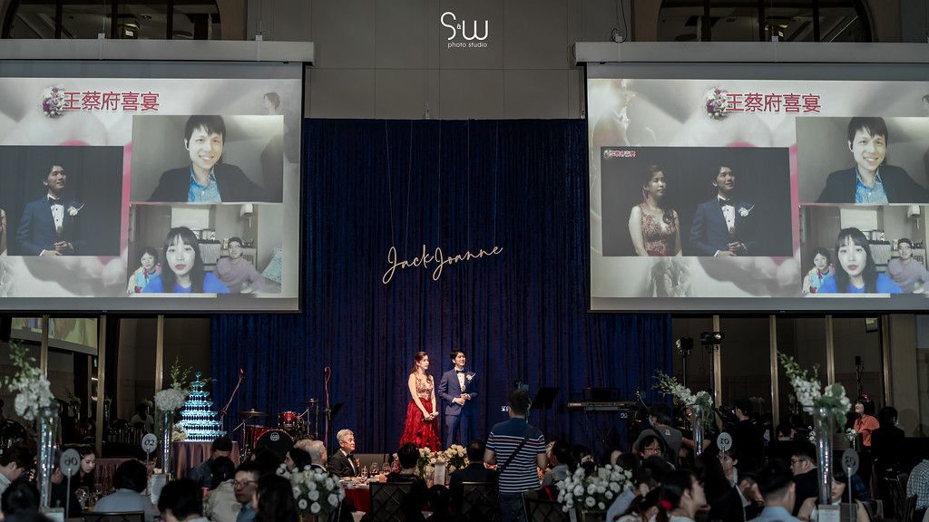 Wedding reception with live performance displayed on large screens above stage.
