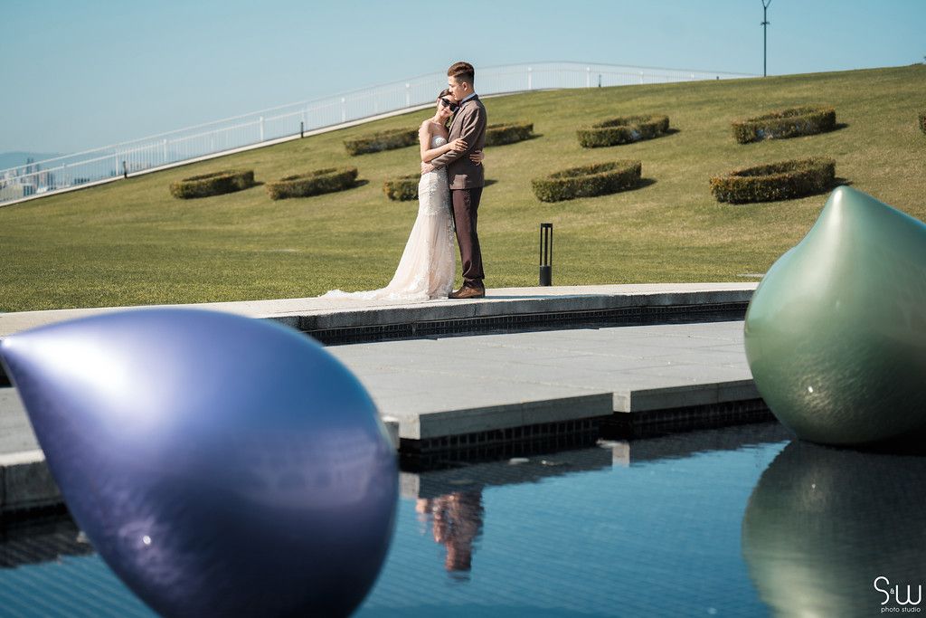 Wedding couple embracing by a modern pool with decorative spheres.