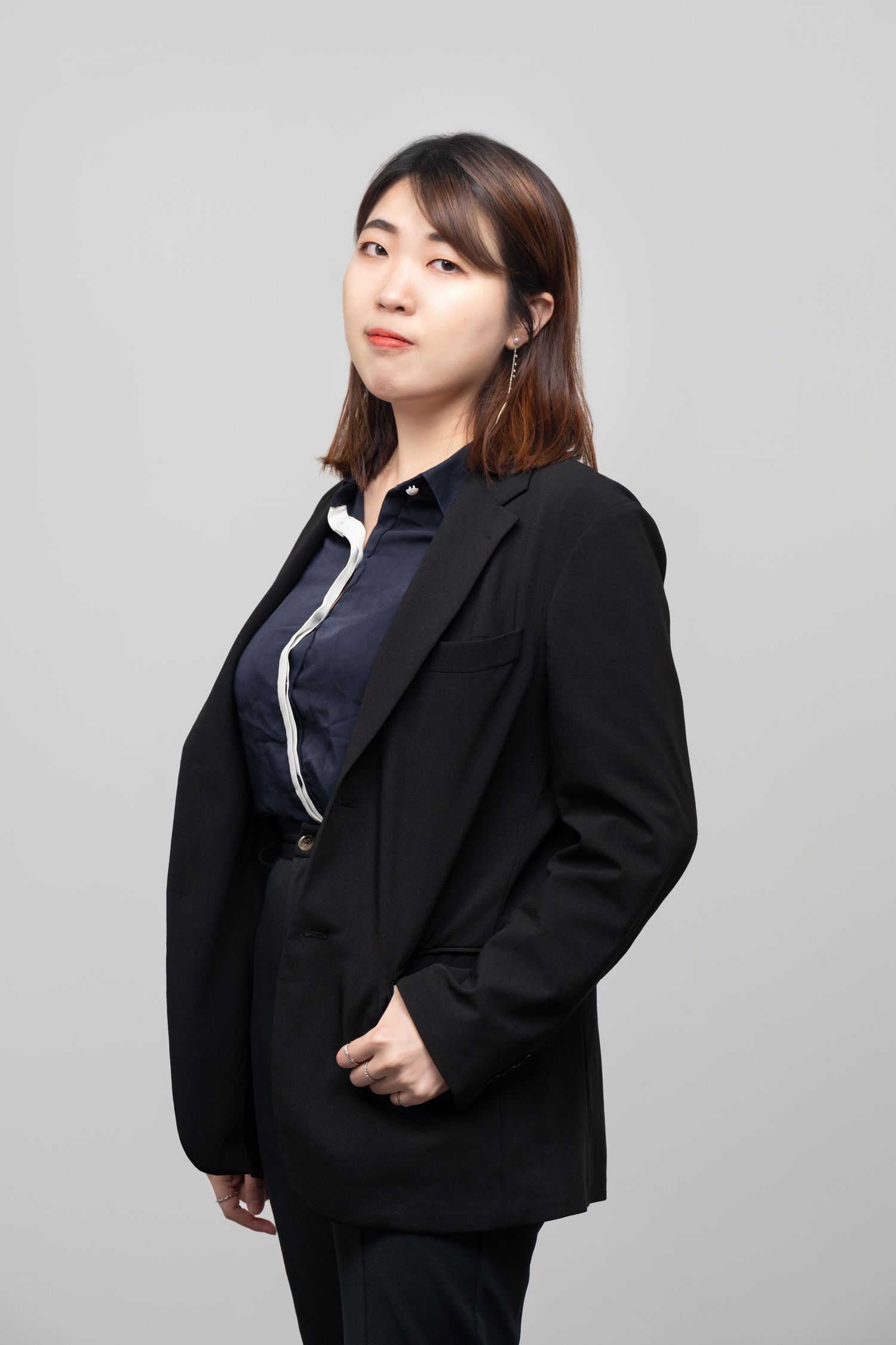Professional studio portrait of someone wearing a black blazer and navy shirt against a gray background.