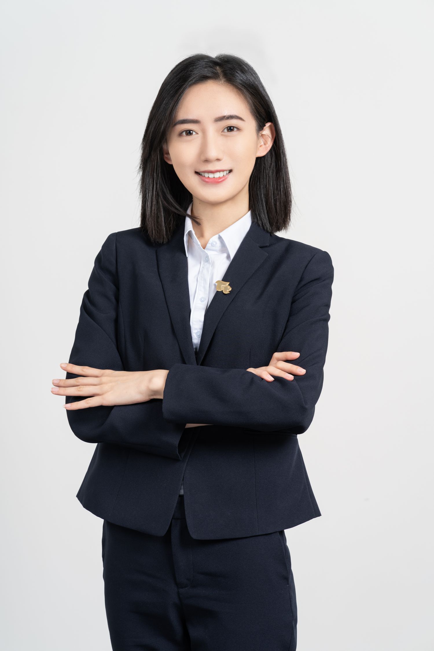 Professional business portrait of person in navy suit with crossed arms standing against light gray background.