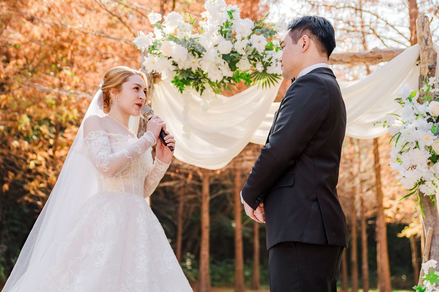 Newlyweds share a romantic moment under a floral arch adorned with white blossoms during an autumn outdoor ceremony.