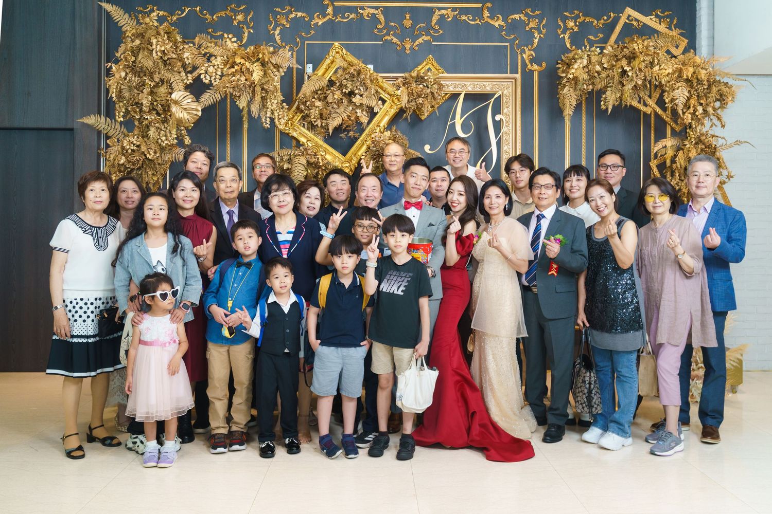 A group photo at an elegant event with gold decorative backdrop and formal attire including red and beige evening gowns.