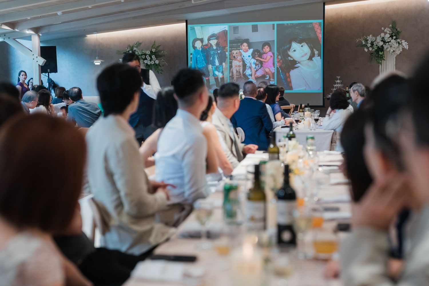 Business meeting in a conference room with attendees seated around a long table with drinks and a projection screen visible.