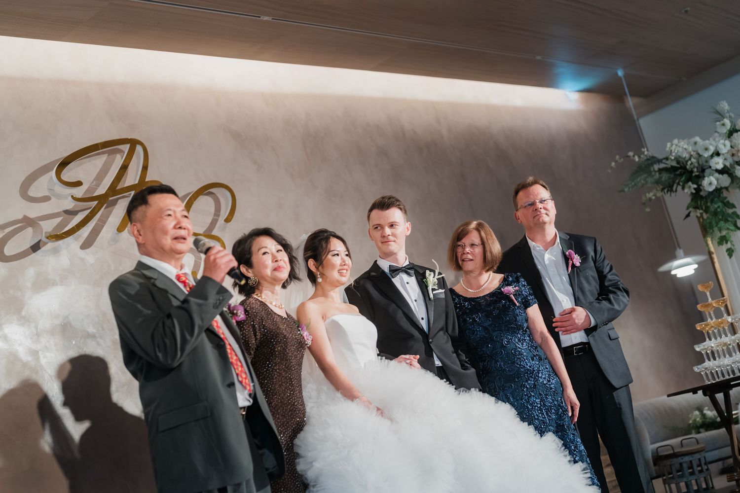 Wedding guests celebrate and laugh together during a candid reception moment at an indoor venue.