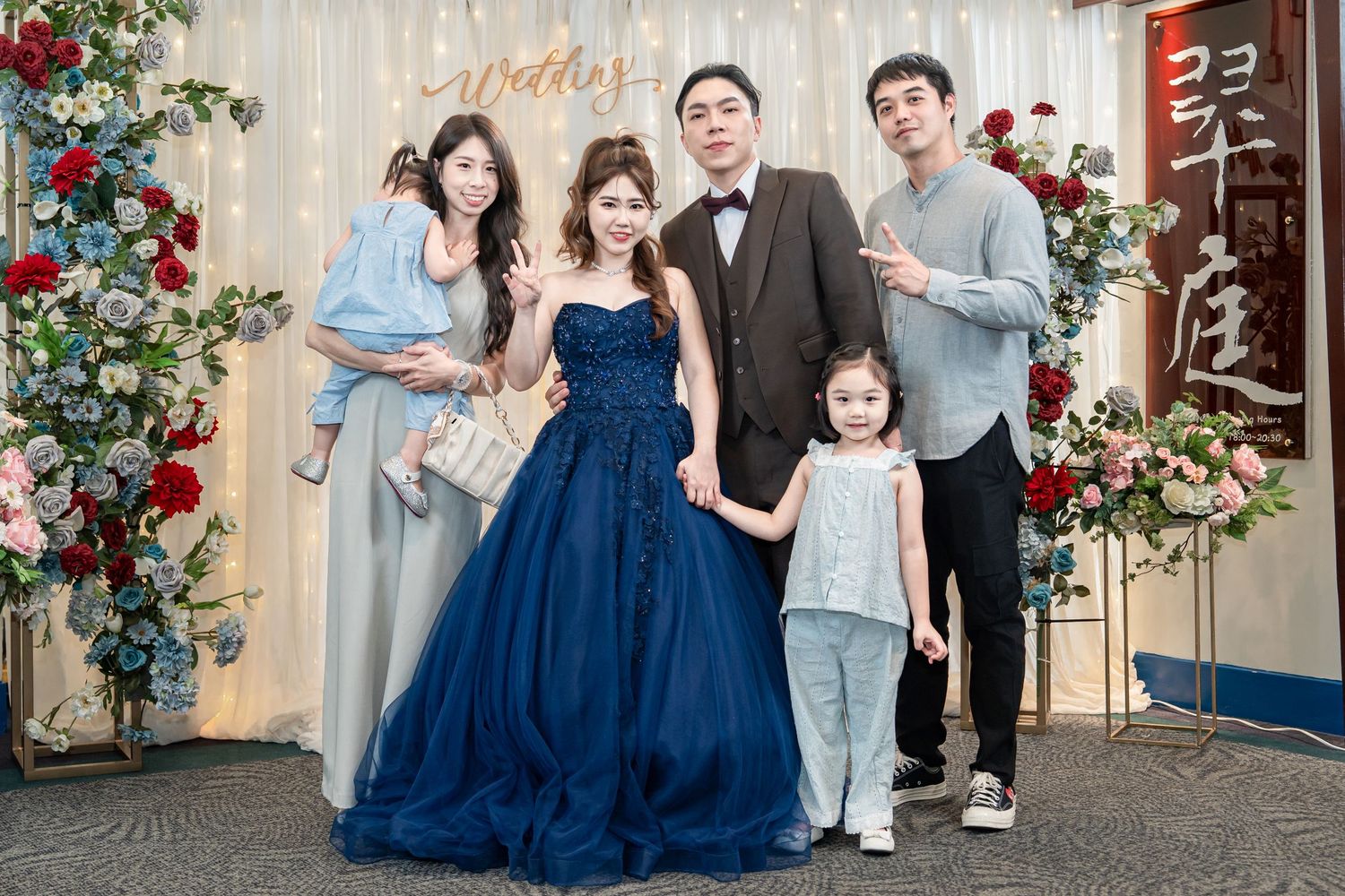 A family wearing coordinated navy blue and grey outfits poses together for formal portraits with floral decorations.