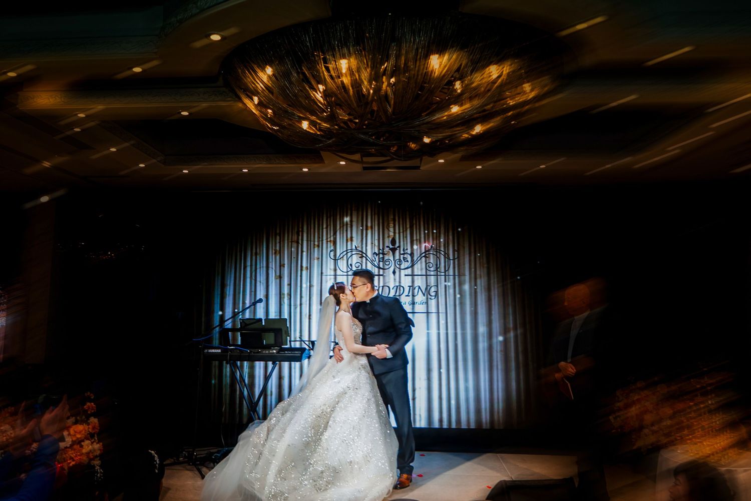 A couple shares a romantic dance together in a dimly lit venue with dramatic lighting and curtains in the background.