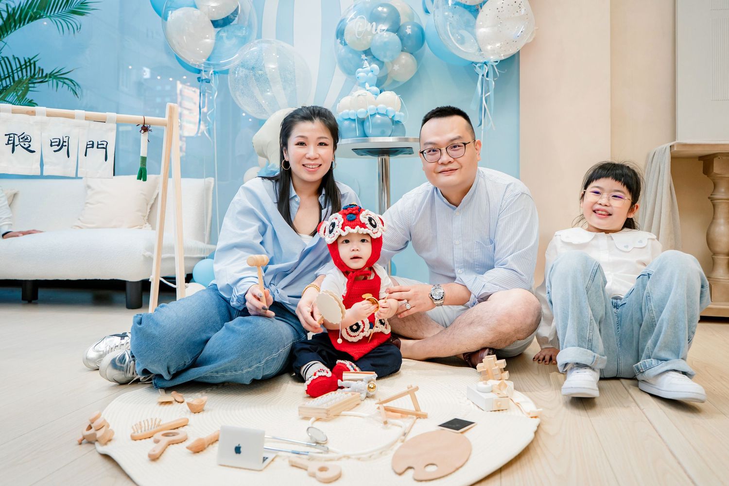 Family members lie on floor playing together with toys and books in a bright living room setting.