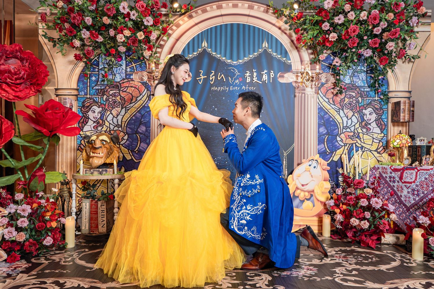 A couple in Beauty and the Beast costumes pose during a romantic proposal surrounded by roses and stained glass decor.
