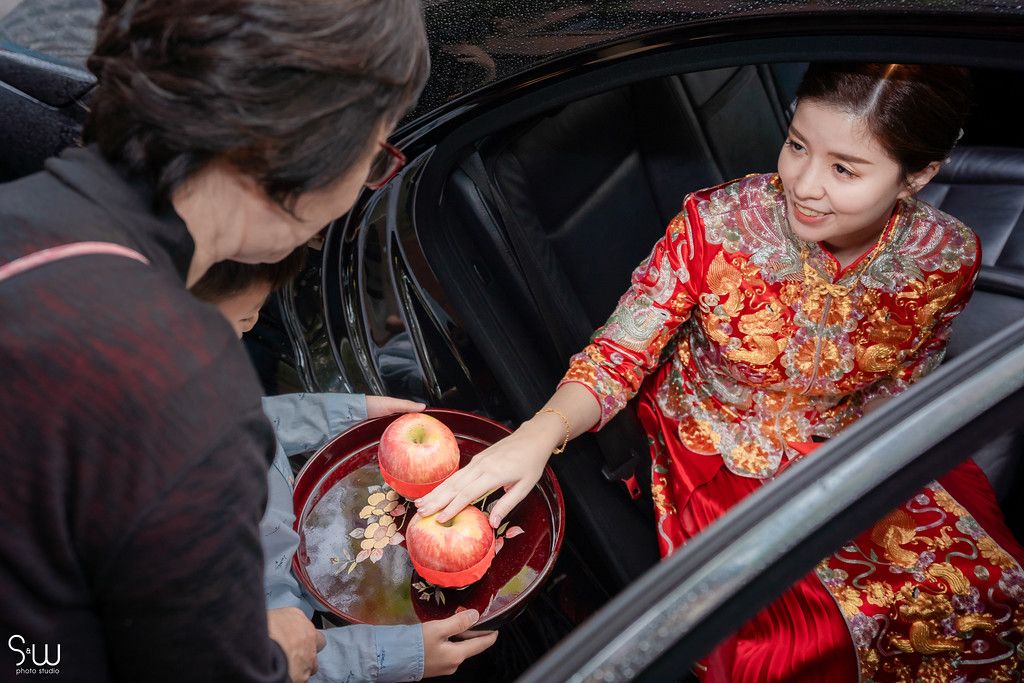 Bride in traditional red cheongsam receiving gifts during Chinese wedding ceremony.