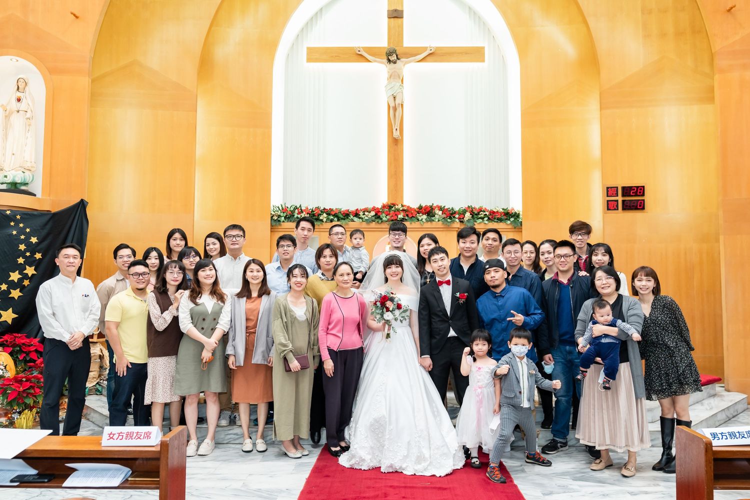 Wedding celebration group photo in front of church altar with decorative floral arrangements.