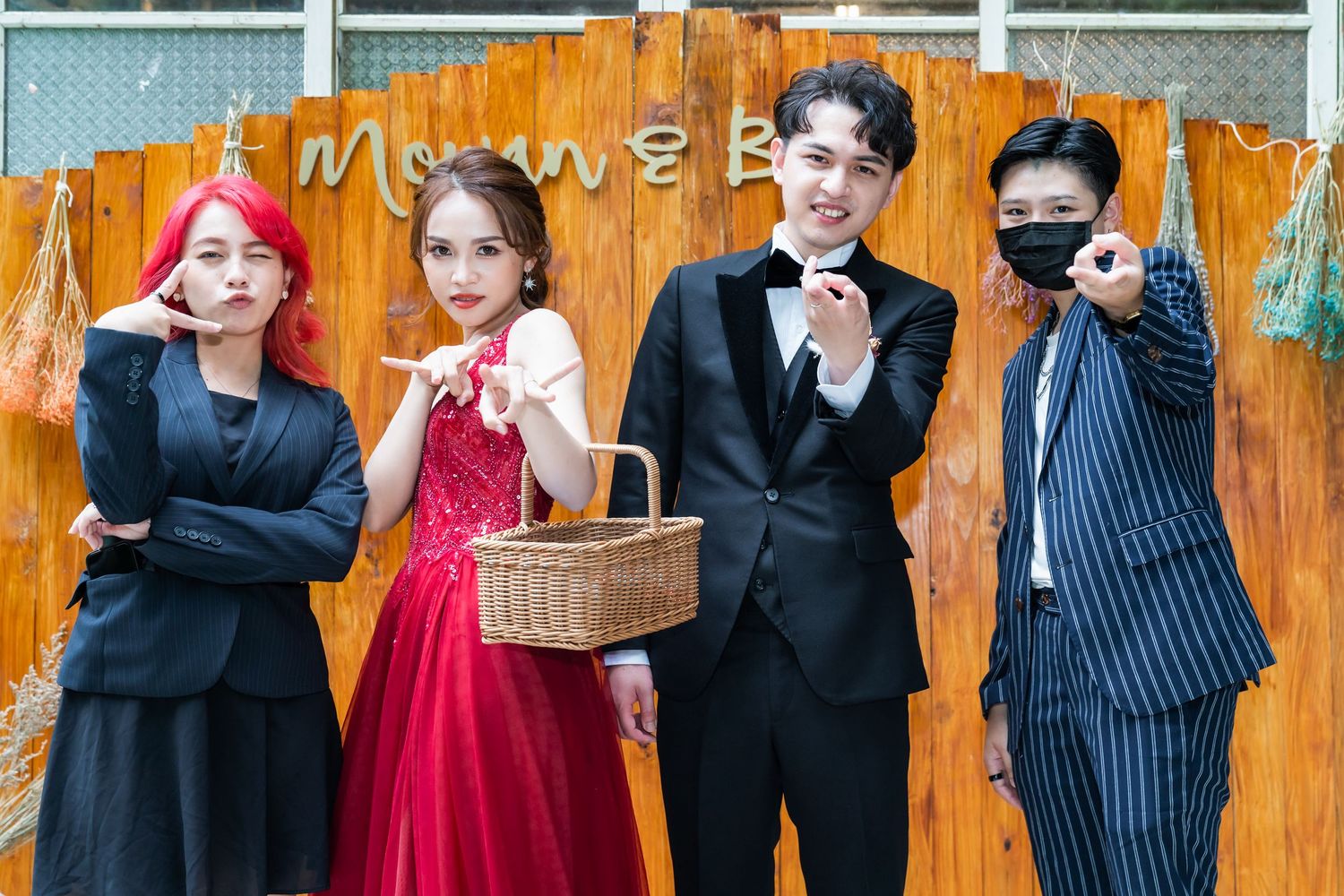 A group strikes playful poses in formal attire against an orange backdrop.