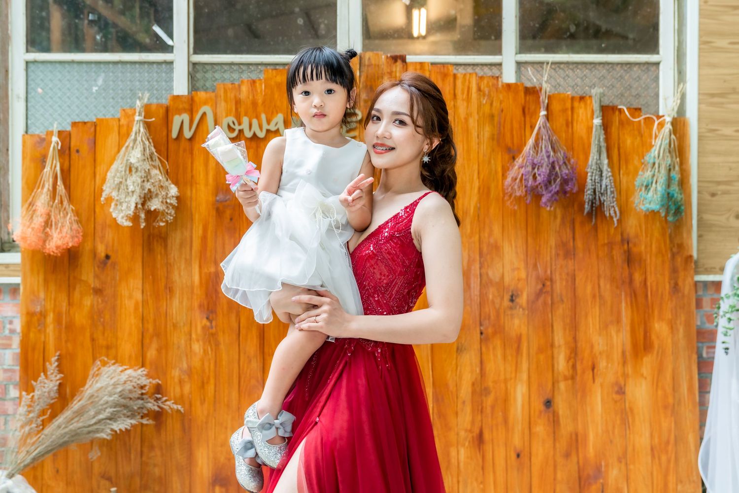 A stunning red formal dress photoshoot scene against a rustic wooden backdrop with decorative dried flowers.
