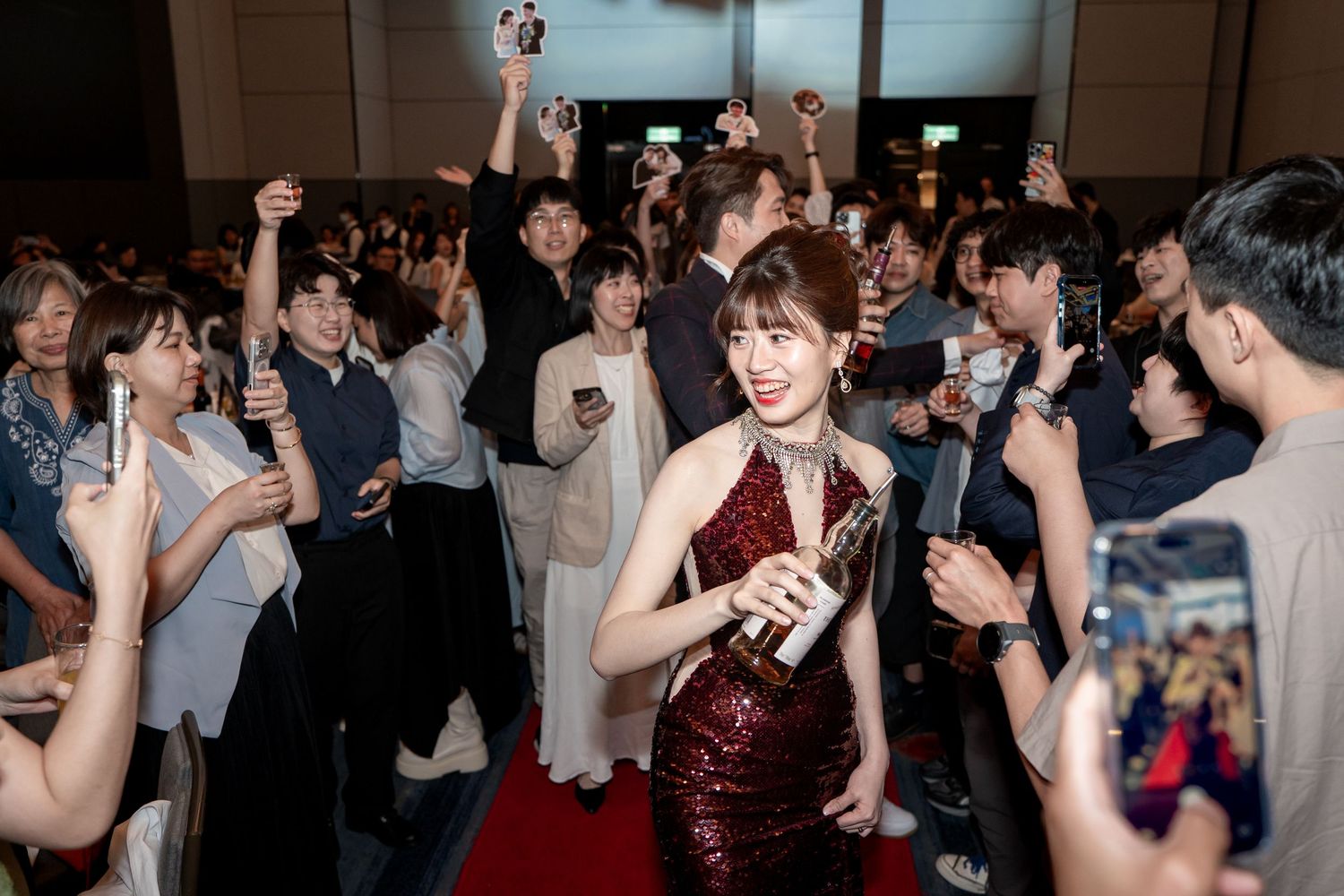 Woman in red sequin dress holds award on red carpet surrounded by cheering crowd at formal event.