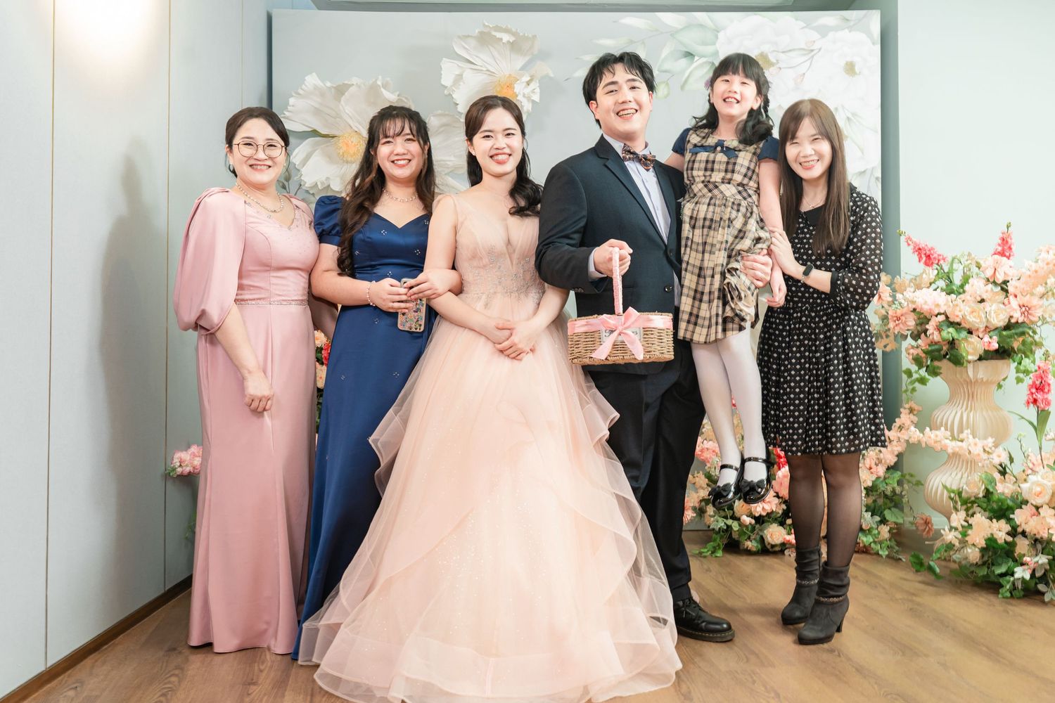 A group of people in formal attire pose together at an elegant event with floral decorations.