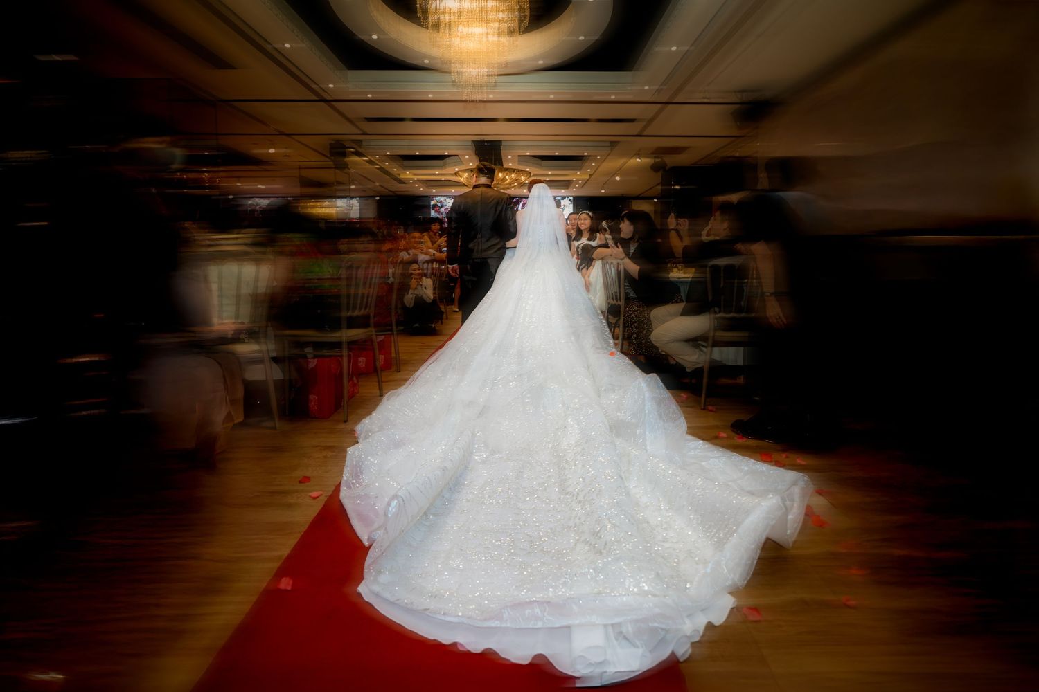 A bride in a flowing white wedding gown twirls gracefully on a wooden dance floor in an elegant ballroom setting.