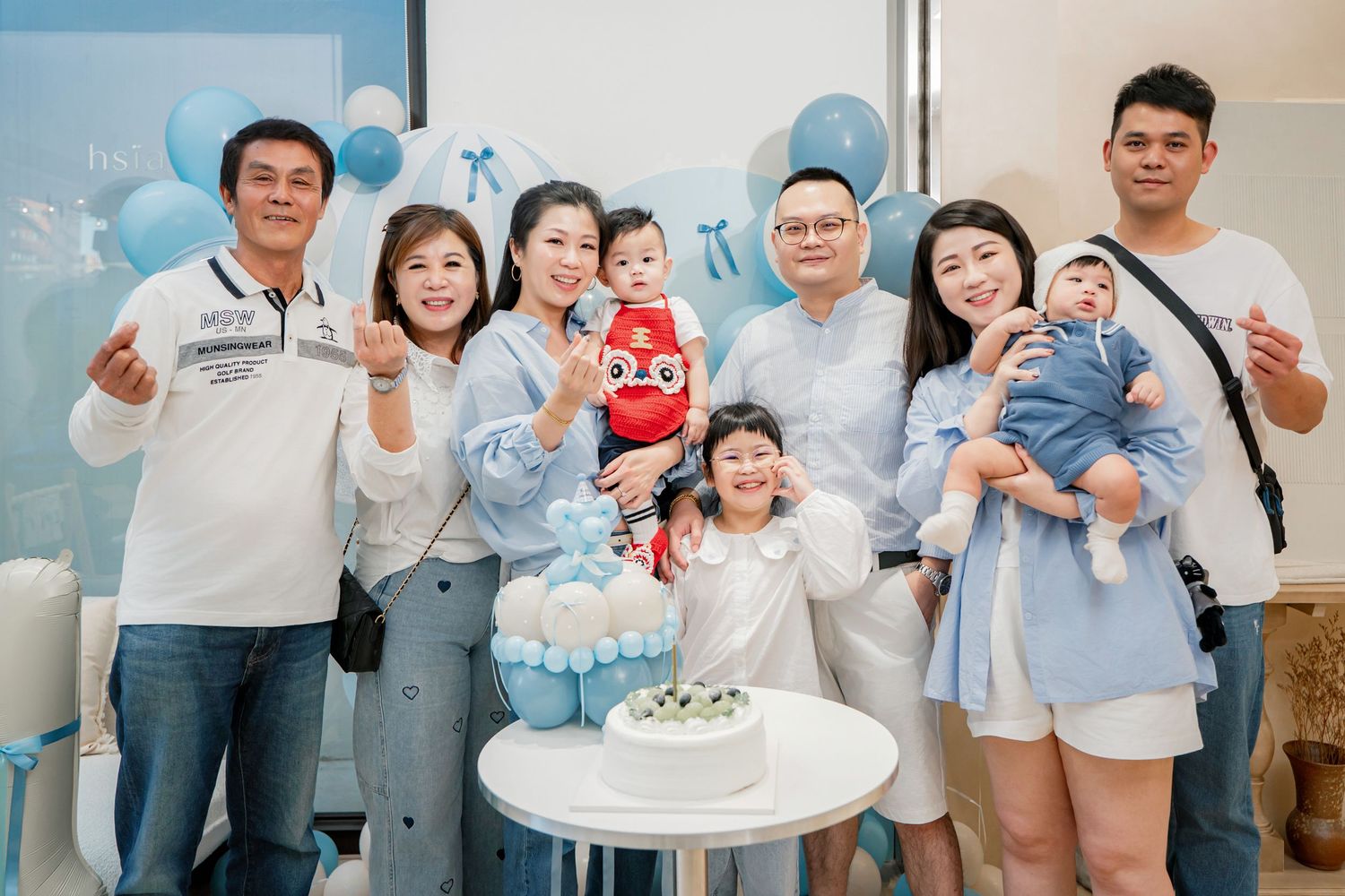 A group of people in light blue and white clothing gather together for a casual indoor celebration.
