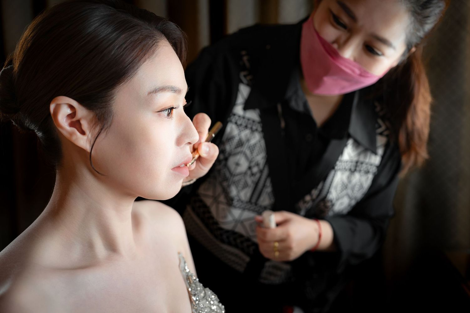 Makeup artist applying pink lipstick on client during professional beauty session.