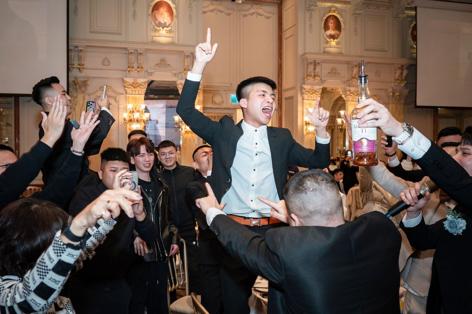 People at a crowded party raise their drinks in celebration while wearing protective face masks during an indoor gathering.