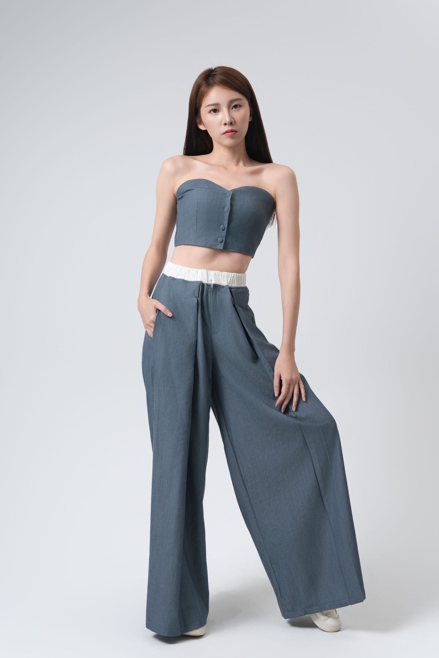 Model wearing a modern two-piece outfit with wide-leg gray palazzo pants and matching crop top in studio setting.