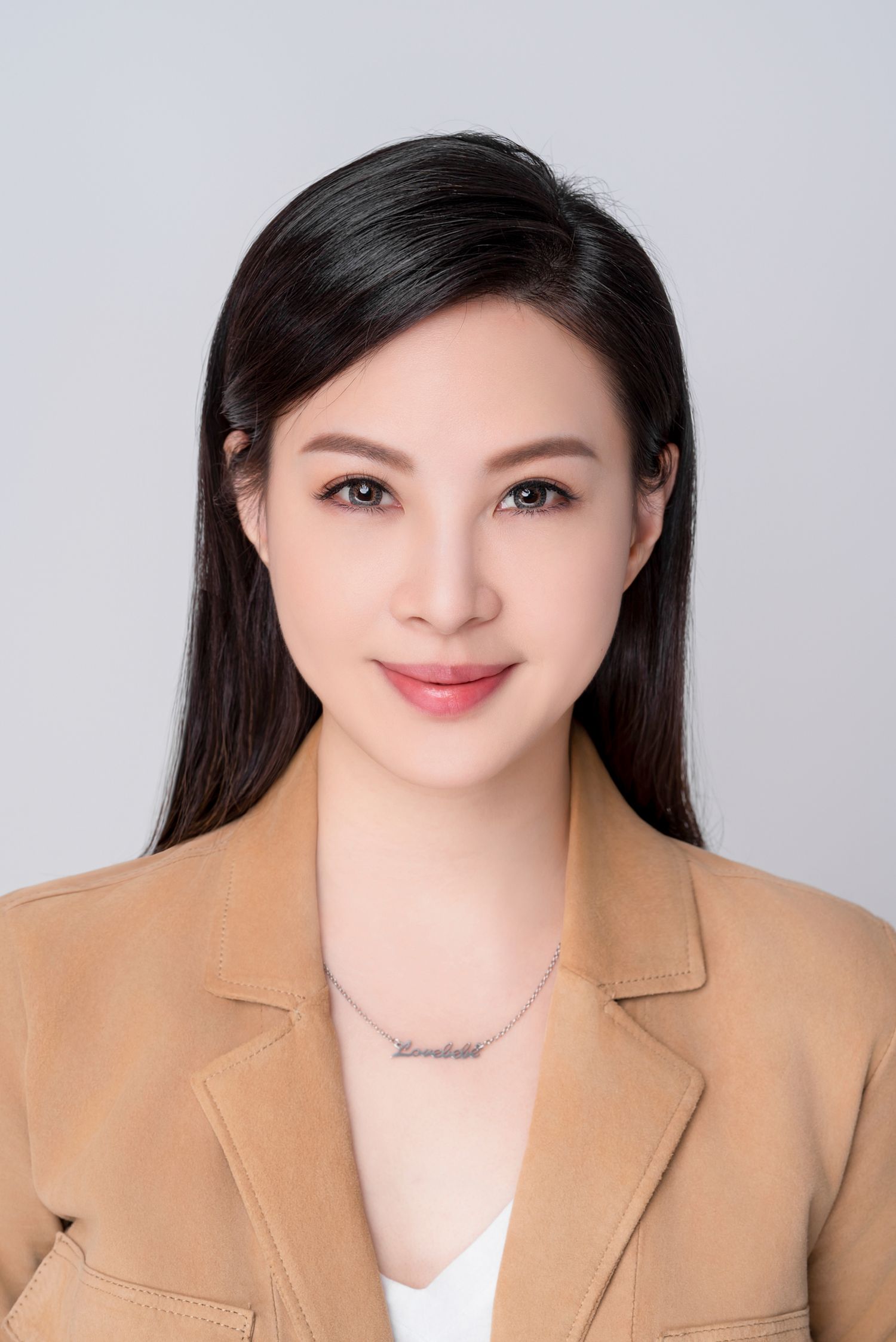 Professional headshot of someone wearing a tan blazer and white top against a light gray background.