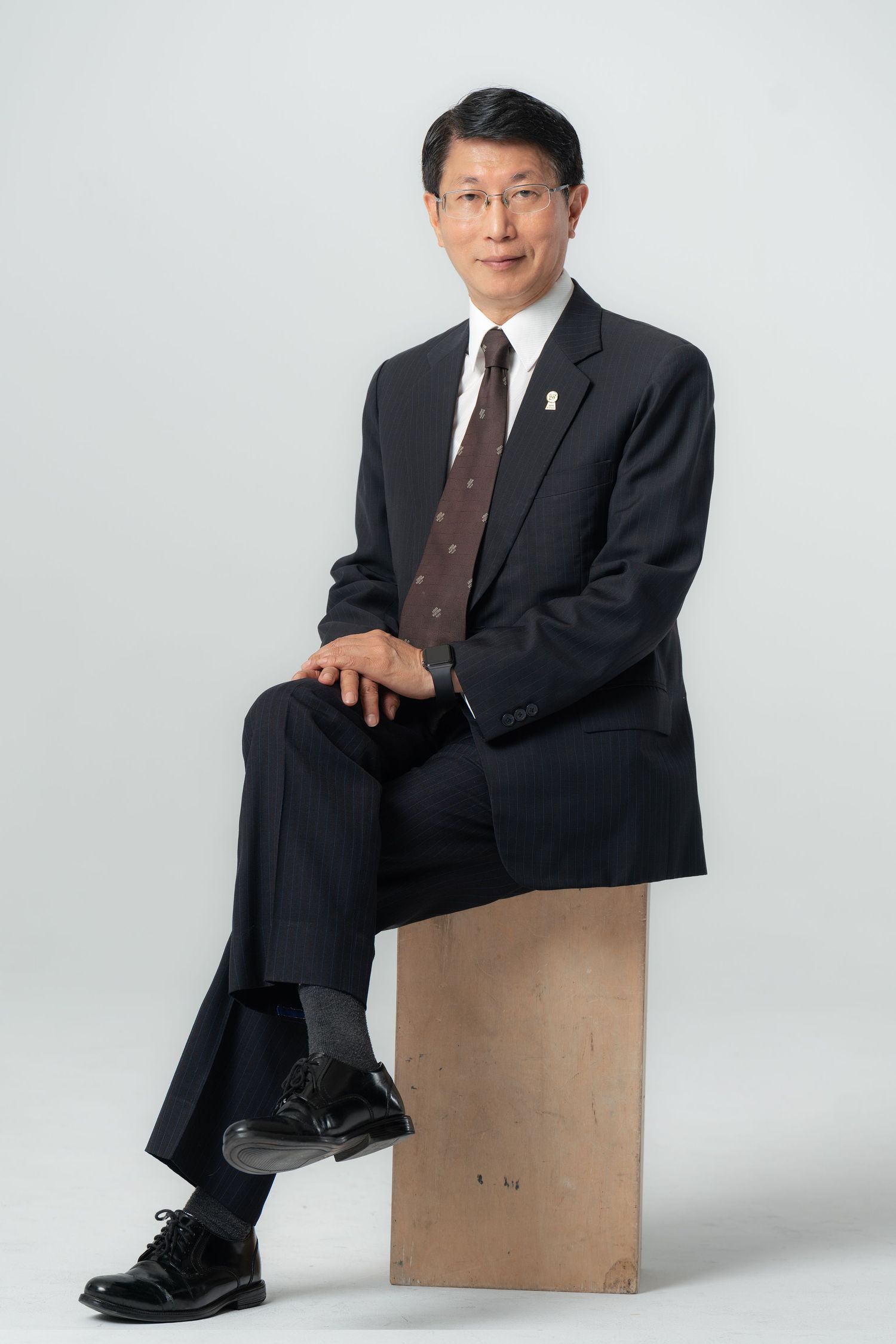 A person in a dark business suit sits on a wooden box in a series of professional studio portrait poses against a white backdrop.