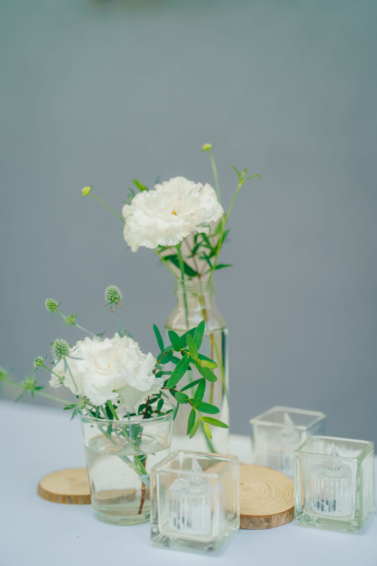 Elegant white carnations arranged in clear glass vases with green stems against a soft blue-grey background.