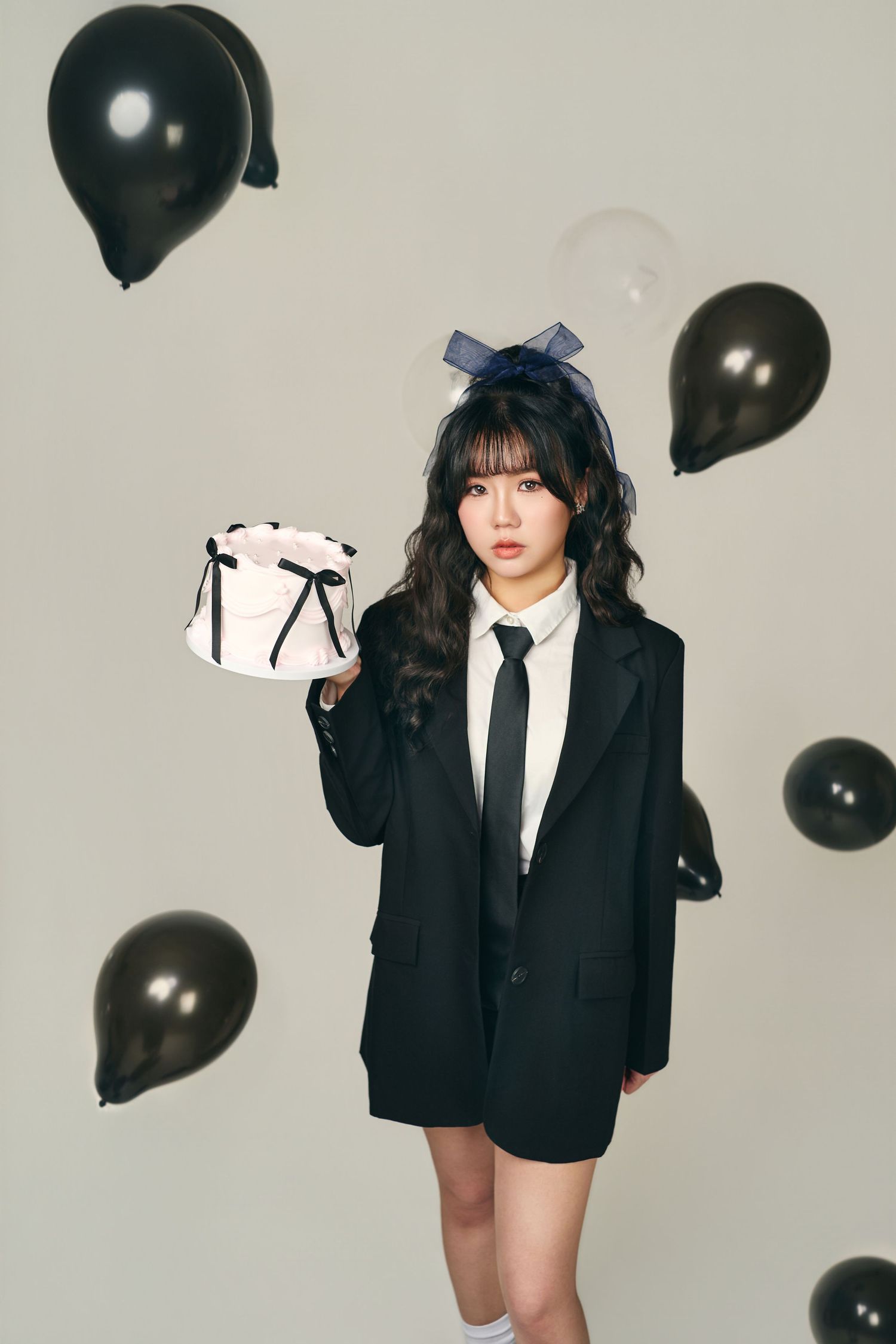 Fashion photoshoot with black balloons featuring dark blazer and tie against light background.