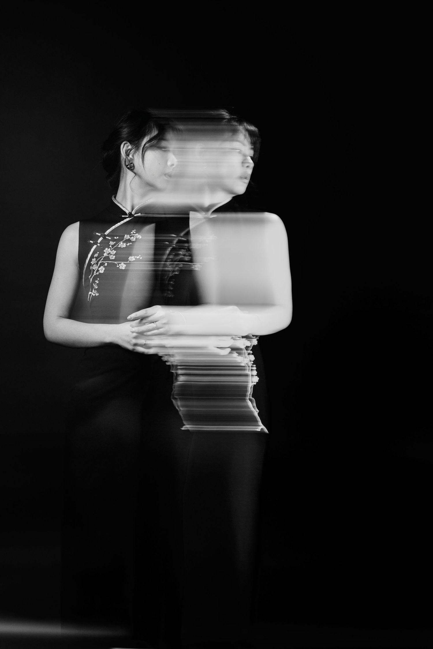Black and white long exposure photo of a woman in a floral qipao, creating a ghostly motion blur effect.