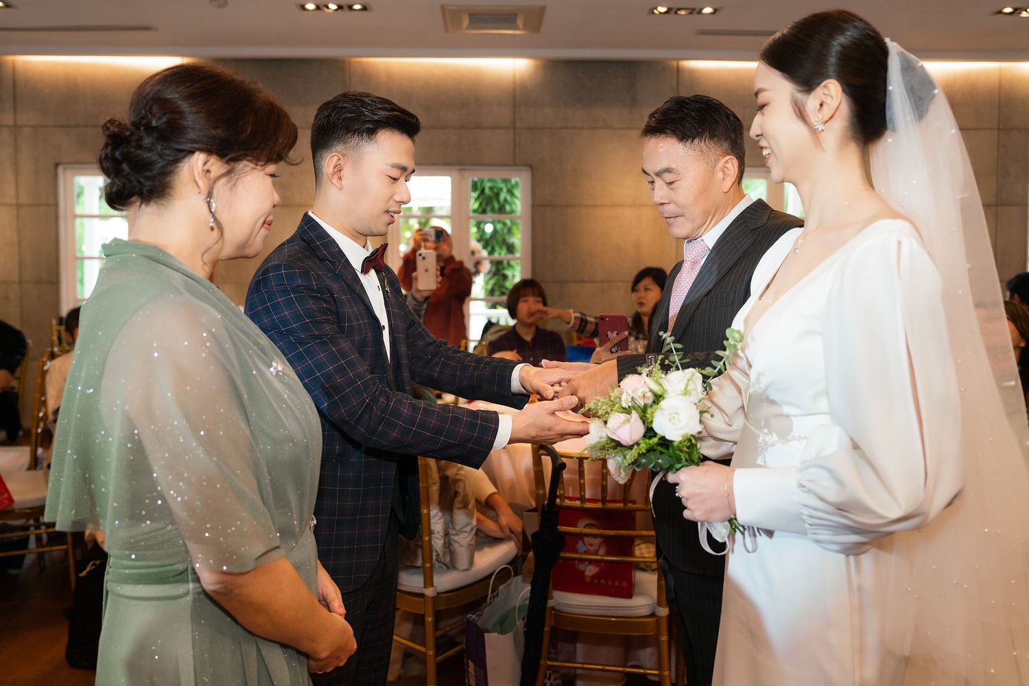 A wedding ceremony moment shows a formal gathering with traditional customs and white floral bouquet at an indoor venue.