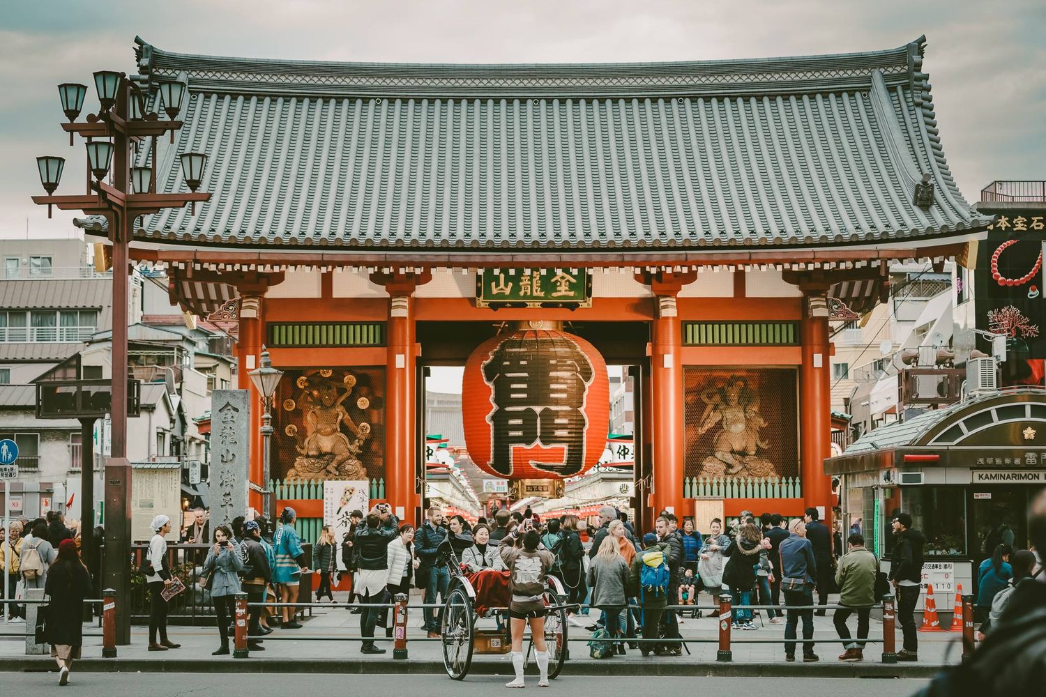 Tourists gather at the iconic Kaminarimon Gate entrance of Sensoji Temple in Asakusa, Tokyo, featuring its large red lantern.