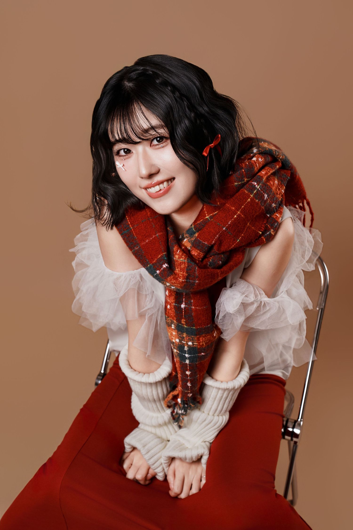 A violinist in a white ruffled blouse and red dress poses with their instrument against a brown backdrop.