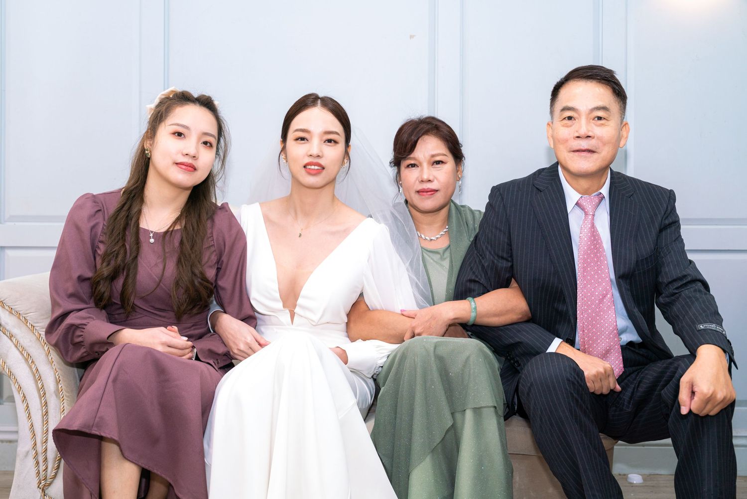 A group sits together on formal occasion wearing elegant attire in burgundy, white, sage green and navy suits.