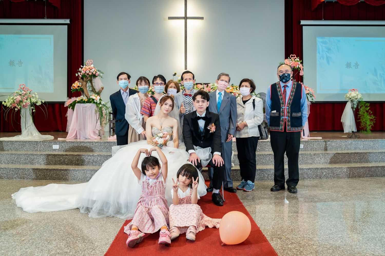 Wedding party poses for formal photo on church steps with cross and floral decorations.