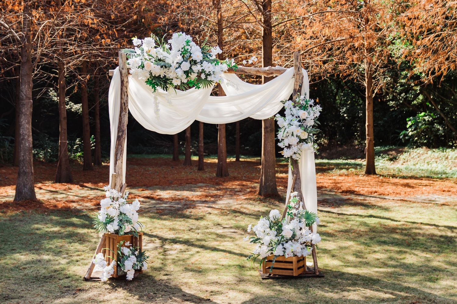 White draped wedding arch decorated with fresh flowers and greenery in an autumn outdoor setting.
